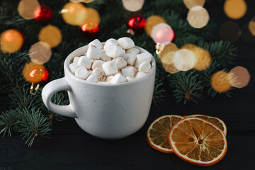 Tasty hot cocoa drink with marshmallows in cup and dry orange slices on black table, closeup