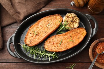 Halves of tasty cooked sweet potato in baking dish served on wooden table, flat lay