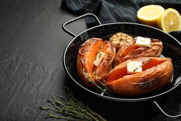 Tasty cooked sweet potatoes with feta cheese, garlic, thyme and lemon on black table, closeup. Space for text