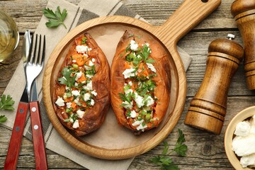 Tasty cooked sweet potatoes with feta cheese, green onion and parsley served on wooden table, flat lay