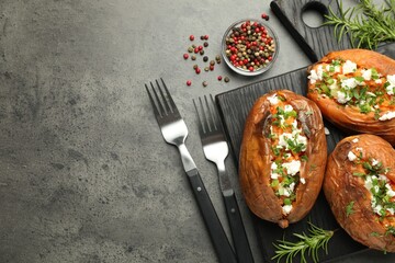 Tasty cooked sweet potatoes with feta cheese, green onion and parsley served on gray textured table, flat lay. Space for text