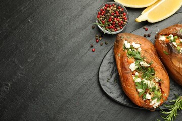 Tasty baked sweet potato with feta cheese, lemon, peppercorns and herbs on dark textured table, flat lay. Space for text