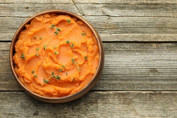 Tasty mashed sweet potato with thyme in bowl on wooden table, top view. Space for text