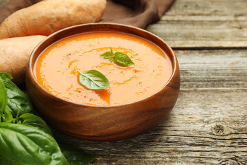 Delicious sweet potato soup, fresh vegetables and basil on wooden table, closeup