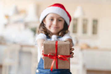 Focused close up shot of little Santa`s helper. Caucasian small kid child girl holding Christmas present gift box looking at camera, celebrating Christmas New Year at home