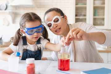 Playful mother and little daughter girl in protective wear having fun playing with chemistry lab...