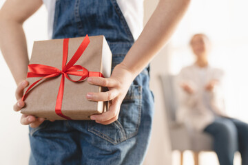 Focused shot of little small girl daughter giving present gift box making surprise to her mother on Birthday Christmas Mother`s day, hiding present behind at home