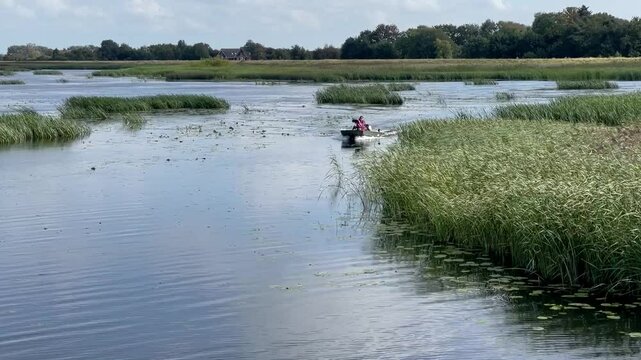 Small motorboat with two passengers driving by between reet islands in an estuary in the Wadden Sea National Park