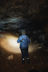 A solitary individual stands in a mysterious cave, illuminating their surroundings with a bright flashlight, creating a stunning contrast against the oppressive darkness on their adventurous journey