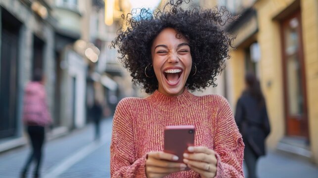 A woman jumping up and down while looking at her phone, with a big smile, thrilled by the content she&acirc;&euro;&trade;s just seen 