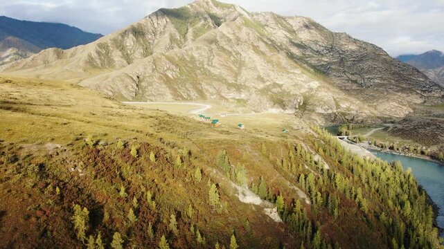 Sunlight gliding over a mountain valley showcases a turquoise river winding through the landscape, accompanied by buildings lining the riverbank