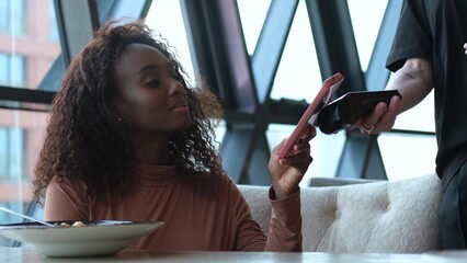 A customer uses her smartphone to make an electronic payment and pay her bill at a cafe. A very...