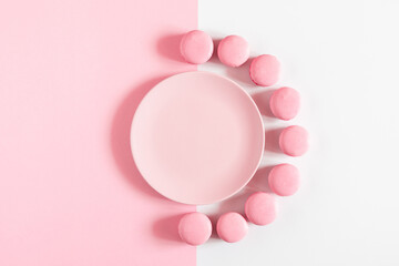 Top view of empty pink plate, pink macaroons on white and pink background. Sweets concept.