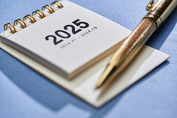 small 2025 desktop calendar with pen on blue background