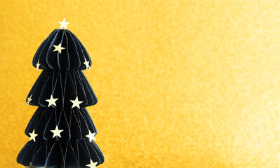 A black paper tree with stars on it is on a gold background. The tree is decorated with stars and is placed on a table