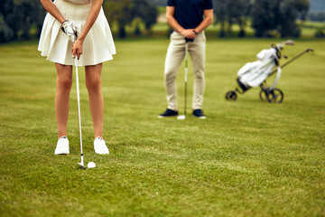 A young golfer practices putting on a green course with a supportive companion, enjoying time