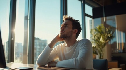 Confused man sitting in a modern office with large windows, looking at his computer screen with a perplexed look, sunlight filtering through the windows