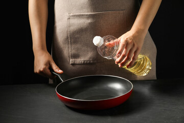 Woman with bottle of oil and frying pan at dark gray textured table, closeup