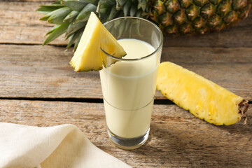 Tasty pineapple smoothie in glass and fruit on wooden table, closeup
