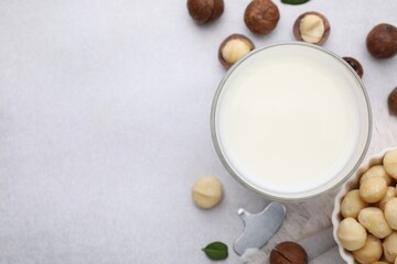 Glass of macadamia milk and nuts on white table, flat lay. Space for text