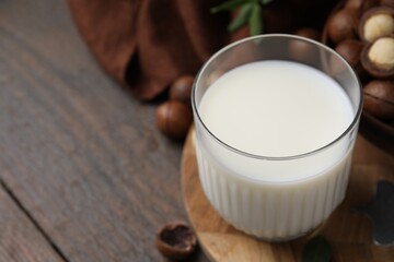 Glass of macadamia milk and nuts on wooden table, closeup. Space for text