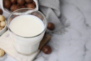 Glass of macadamia milk and nuts on white marble table, closeup. Space for text