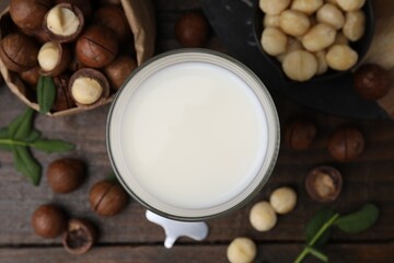 Glass of macadamia milk and nuts on wooden table, flat lay