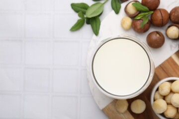 Glass of macadamia milk and nuts on white tiled table, flat lay. Space for text