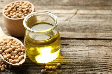 Cooking oil in jar and soybeans on wooden table, closeup. Space for text