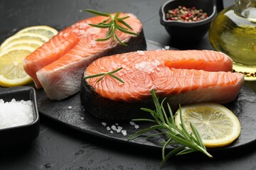 Fresh raw salmon steaks with salt, lemon and rosemary on dark textured table, closeup