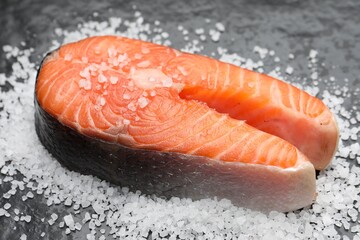 Fresh raw salmon steak with salt on dark textured table, closeup
