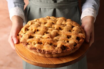 Woman holding wooden board with tasty homemade apple pie on light coral background, closeup