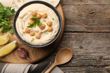 Delicious hummus with chickpeas and pita served on wooden table, flat lay. Space for text