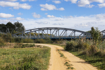 Metal bridge background. Road bridge construction. Empty asphalt road. Blue sky weather long bridge over Narew river. Tykocin village in Poland. Steel structure landscape. Wild nature along the river.
