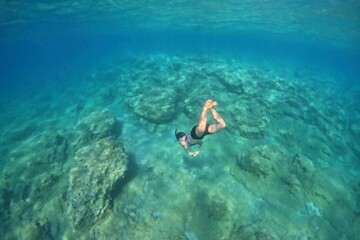 Young girl swimming underwater from the sea surface, in the warm clear calm ocean. Rocky seascape...