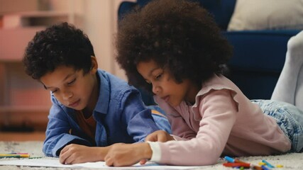 Two African American siblings drawing pictures while lying on the floor, fun