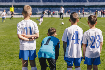 Fototapeta premium Boys Play Soccer Match. Group of Children Sport Team. Soccer Background. Youth Sports Team Players Together. Football Game For Children. Kids on Bench Watching Tournament Game. Football Stadium