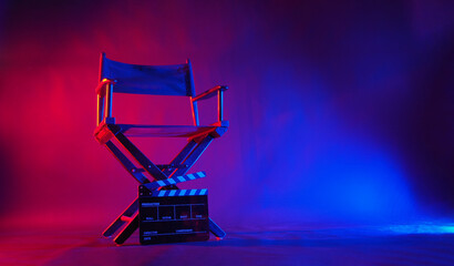 Black Director chair and clapper board in red and blue light color with black background.