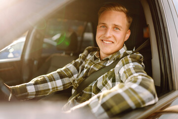 Young man in a car smiling and looking at the camera. Buying and renting a car. Car travel, lifestyle concept.