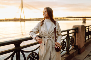 Fototapeta premium A young woman walks along the embankment and enjoys the warm autumn sunset. Lifestyle, travel, tourism, active life.
