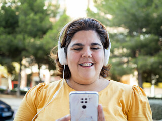 A cheerful woman with intellectual disability listening to music on her headphones. She smiles as...