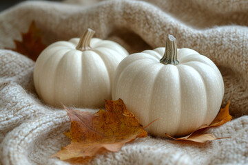 A minimalist aesthetic featuring small white pumpkins, a beige wool blanket, and dried autumn leaves scattered on a wooden surface.
