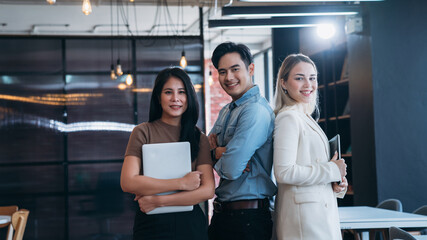 Three people are standing together in a room, with one of them holding a laptop