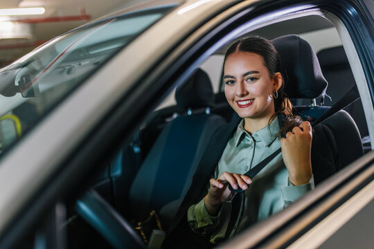Young businesswoman putting a seatbelt on. Ready to drive off from his parking spot in an underground garage.