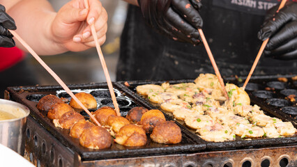 Close-up of hands cooking Takoyaki, a popular Japanese street food, on a traditional pan. Ideal for food, street market, or Asian cuisine-themed projects.