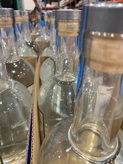 A detailed close-up shot of clear glass bottles, tightly arranged in cardboard packaging. The transparent bottles feature wooden cork stoppers sealed with a silver-colored foil.