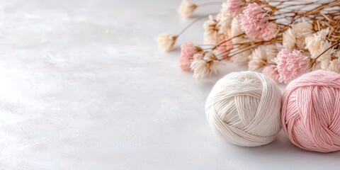 balls of yarn in neutral shades lie next to knitting needles and dried flowers on a bright surface, 