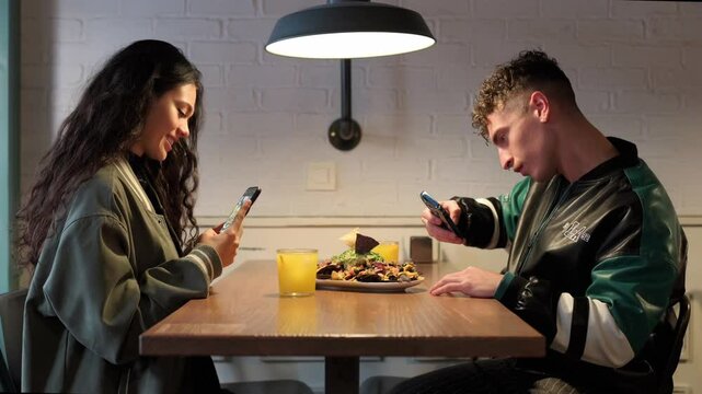 couple in a restaurant taking pictures with their smartphones of a plate of Mexican nachos before eating. Food influencers in a restaurant creating content.