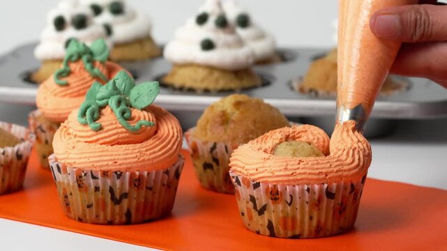 Halloween food, hands forming a pumpkin with orange frosting on a halloween cupcake
