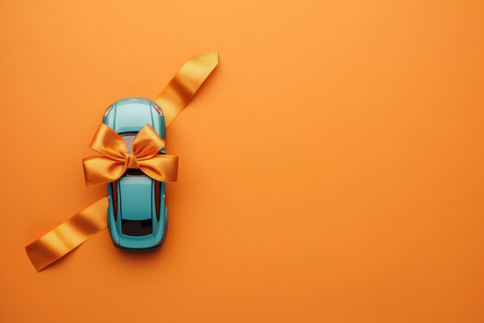 Toy car wrapped with golden ribbon on vibrant orange background
